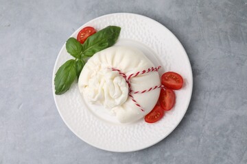 Delicious fresh burrata cheese with basil leaves and tomato on grey table, top view