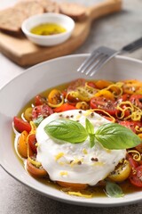Delicious fresh burrata salad in bowl served on gray textured table, closeup