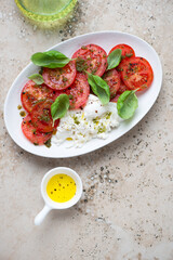 Fresh tomatoes served with basil oil and burrata, top view on a beige granite background, vertical shot with space