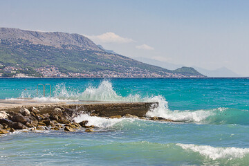 shore of the blue sea with big waves and mountains in the background