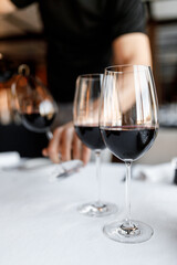 handsome bartender skillfully pours red wine into a glass on a beautiful white tablecloth in a nice restaurant