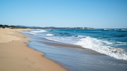 Gentle waves crash on a sunny beach, creating a peaceful atmosphere. The clear sky complements the stunning landscape, perfect for summer travel and relaxation