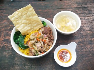 A bowl of noodles with slices of beef with sambal matah and pakcoy vegetables, served with fried wonton crackers, chili oil and wonton soup