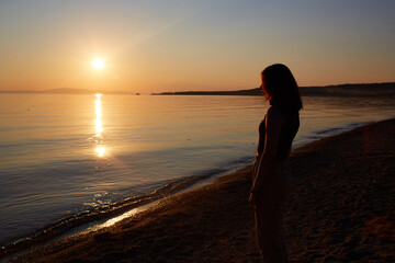 A pretty girl enjoys the sunset on a sandy beach. Summer travel, vacations at sea. 