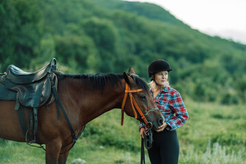 Obraz premium Happy blonde with horse in forest. Woman and a horse walking through the field during the day. Dressed in a plaid shirt and black leggings.