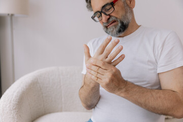 Close-up of arthritis symptoms. Senior man in glasses suffering from pain in hand at home