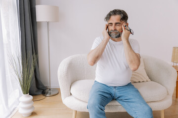 Fototapeta premium Home, senior man and headache on sofa for stress, emotional conflict and temporal vertigo. Living room, couch and old person with pain, migraine and anxiety due overthinking in retirement in house