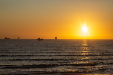 Fototapeta premium Some boats in backlight against orange sky during sunset on the atlantic ocean, taken from Bloubergstrand in the Western Cape of South Africa