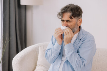 Senior man sneezing into a tissue, experiencing discomfort from cold or allergies, seasonal allergies, virus, flu and sick health, wellness, senior care, and medical treatment for respiratory