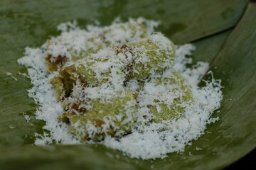 Kue putu in a plate covered with banana leaves in brown background, is a type of traditional Indonesian snack filled with palm sugar, wrapped with grated coconut, and rice flour.