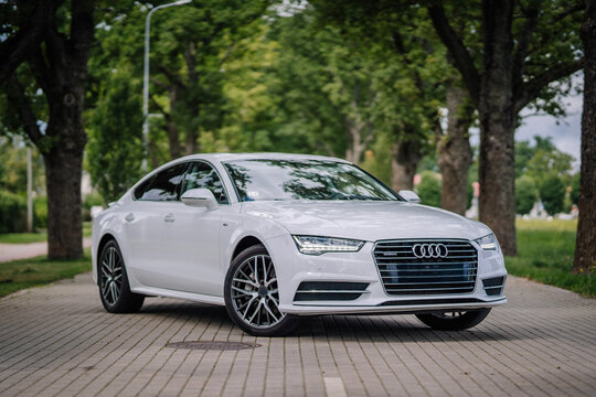 Valmiera, Latvia - August 1, 2024 - A white Audi sedan is parked on a tree-lined street, with greenery in the background, during daylight.