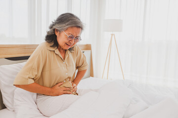 Elderly Asian woman had stomach pain with pained expression on her face while sleeping on the bed,...