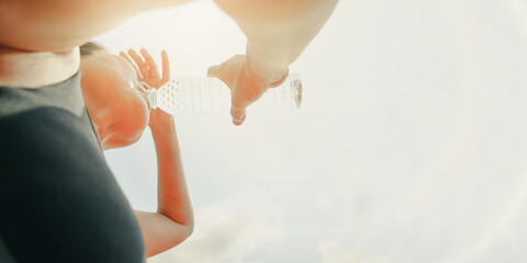 58 year old asian woman exercises under the hot midday sun stand holding bottle of water quench...