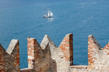 battlements of Malcesine del Garda castle with Lake Garda and a large sailing boat in the background