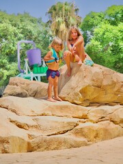 Dos niños trepando a grandes rocas en un parque acuático en un día soleado, disfrutando de la aventura al aire libre.