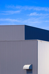 Fototapeta premium Two industrial production and warehouse buildings with HVAC dryer vent on gray and white aluminium corrugated metal wall against blue sky background in vertical frame, perspective side view