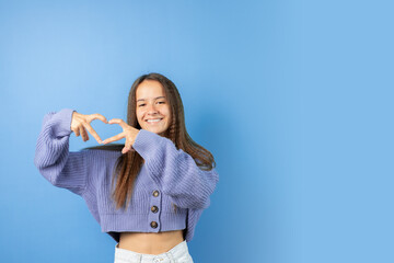 Teenager shows a heart with her hands, teen with a blue background, attractive model in a sweatshirt.