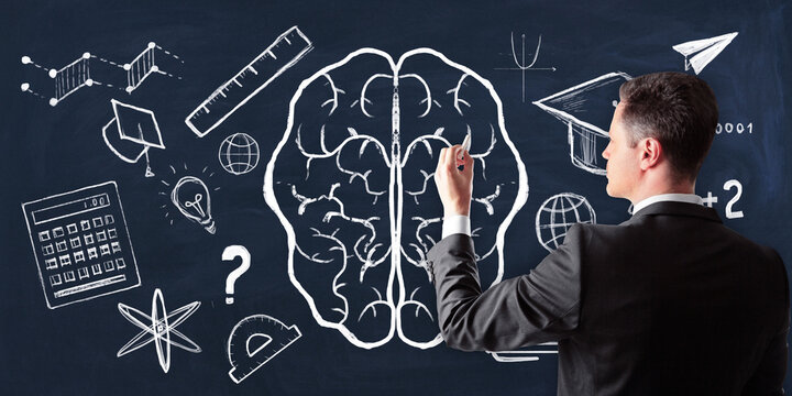Man drawing educational icons and brain outline on blackboard.