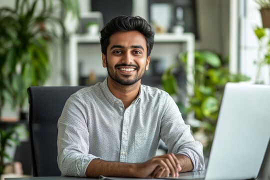Smiling young Indian man sitting in the office at the desk and talking on a video call, making an online recording, conducting training remotely, Generative AI