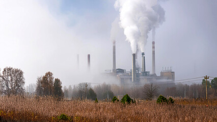 Industrial factory plant with tall smokestacks emitting thick smoke, enveloped in heavy fog. The image highlights the impact of industrial pollution on the environment
