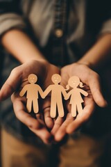 A person is holding three paper cutouts of people, possibly representing a family. Concept of warmth and togetherness, as the person is holding the figures close to their heart
