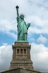 Obraz premium New York, NY, USA - August 4, 2023: Miss Liberty statue frontal view with pedestal, against blue cloudscape