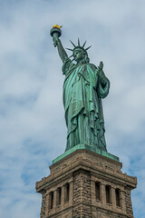 New York, NY, USA - August 4, 2023: Miss Liberty statue from under right, against blue cloudscape