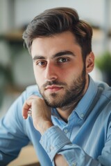 Obraz premium A man with a beard and a blue shirt is sitting on a table. He is looking at the camera with a serious expression