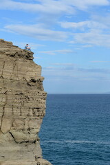 A man is sitting on the edge of the Cape Tobizina cliff. Russian Island. Primorsky Krai