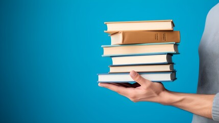 Fototapeta premium Close-up of a Person Holding Tall Stack of Various Books on Blue Background