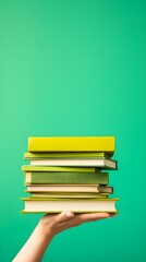 Close-up of a Person Holding Tall Stack of Various Books on Green Background
