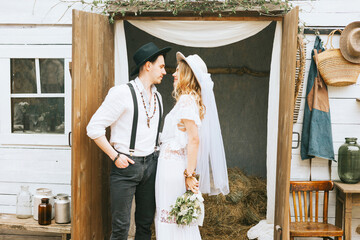 wedding boho style ceremony young couple newlyweds bride in white dress with veil and groom in hat and jeans with suspenders hugging and having fun at barn of country house, shot in motion