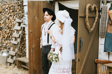 wedding boho style ceremony young couple newlyweds bride in white dress with veil and groom in hat and jeans with suspenders hugging and having fun at barn of country house, shot in motion © klavdiyav