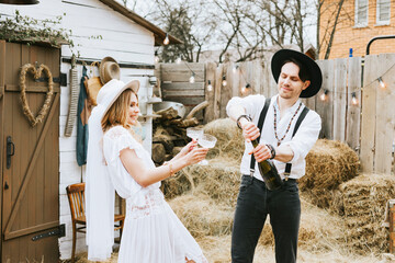 wedding boho style ceremony young couple newlyweds bride in white dress with veil and groom in hat and jeans with suspenders hugging and having fun at barn of country house, shot in motion © klavdiyav