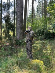 A soldier aiming a rifle.  A soldier with a rifle in his hand standing in the forest.  Dressed in camouflage.