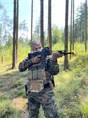 Fototapeta premium A soldier aiming a rifle. A soldier with a rifle in his hand standing in the forest. Dressed in camouflage.