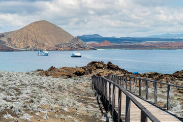 Wooden boardwalk to tranquil bay with sailboats and volcanic hills in background