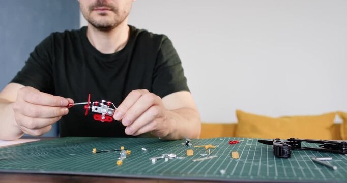 Man screws small plane of metal details sitting at table closeup. Adult in black t shirt makes vintage airplane model at home. Creative hobby