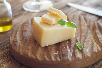 A piece of cheese lies on a wooden board, with a basil leaf on top