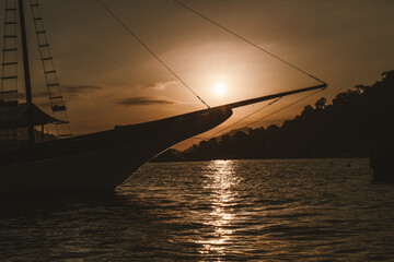 Silhouette of a boat at sunset in Angra dos Reis, Brazil. The sun sets behind the hills, casting a...
