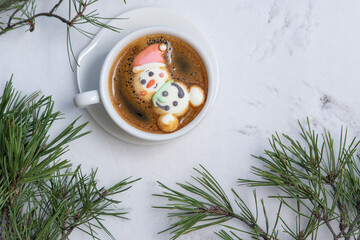 Cup of coffee with marshmallows. Marshmallow snowman in a Santa Claus hat. Winter drink in the snow. Christmas tree. Top view.