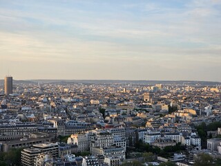 Fototapeta premium Paris, France - April 12, 2024: Aerial view to the city of Paris, during the golden hour between modern skyscrapers and old buildings. Beautiful sunset over the city reflected on the buildings.