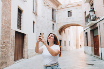 Happy female Tourist taking photos of a historic building in the old town of a European city. A young woman takes pictures of beautiful views of the city on her phone. Travel Explore Europe.