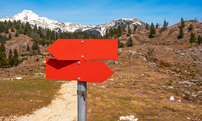 a post with direction indicators in opposite directions in red against the backdrop of beautiful snow-capped mountains
