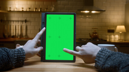 Point of view shot: Close-up of man using green mock-up screen digital tablet computer on the table. Man scrolls and taps on tablet computer in modern kitchen background.	
