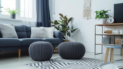 Two knitted poufs near dark blue corner sofa. Scandinavian home interior design of modern living room