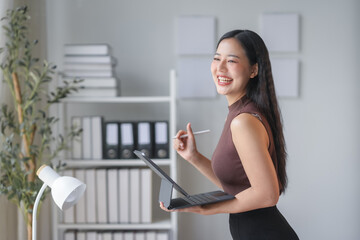 Asian businesswoman is standing in her office holding a tablet and stylus while smiling