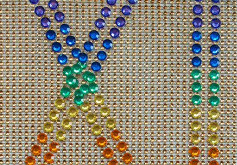 Pattern with beads & grid shows the Roman Numeral 12 or an X with ones or the letter I.  Materials used are faux shiny gems in gold, green, yellow, & orange.
