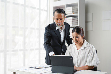 Senior manager is helping a young accountant to use a tablet computer in a luminous office
