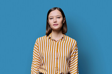 Portrait of young serious woman looking at camera on blue background